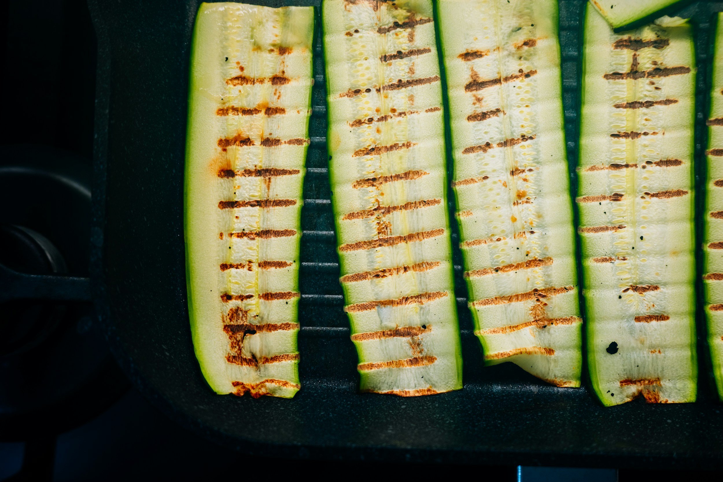 Grilled zucchini slices on a stovetop grill pan, showcasing char marks and a vibrant green color, ideal for healthy recipes and summer grilling.